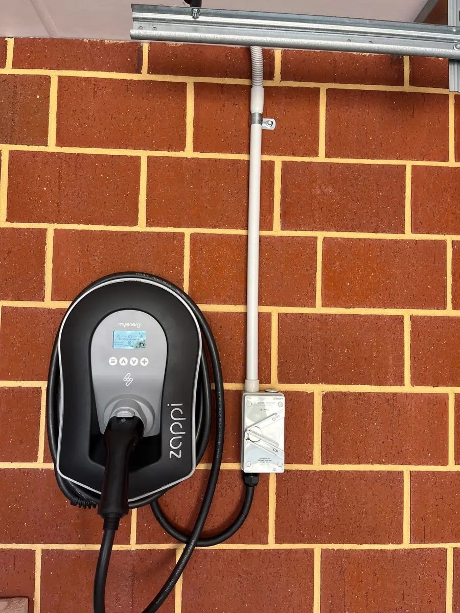myenergi Zappi EV charger on a brick garage wall with isolator